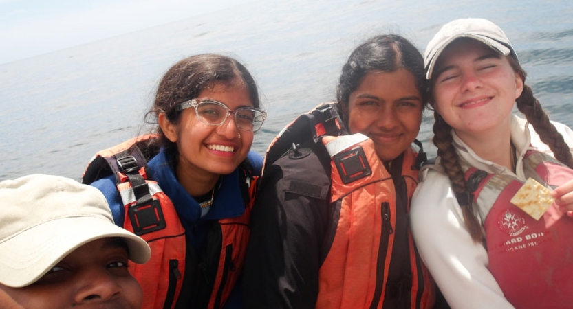 A group of people wearing life jackets smile for the photo. The ocean is behind them. 